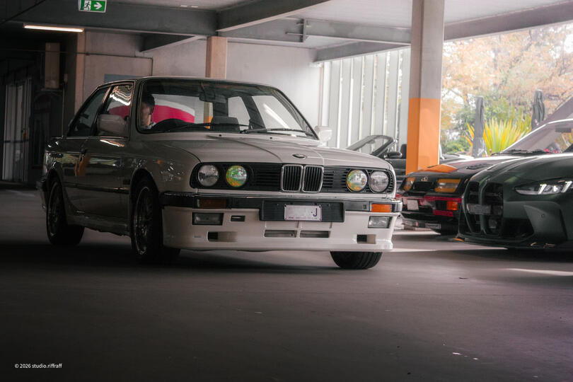 A white BMW 323i driving in a parking garage, lit by the morning light