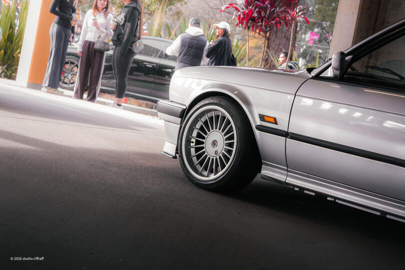 A silver BMW E30 in a parking garage, lit by the morning light