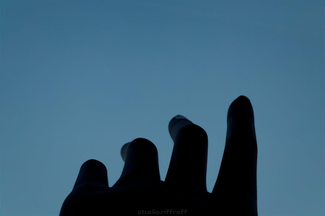 An underexposed hand reaching up towards the sky in front of a window